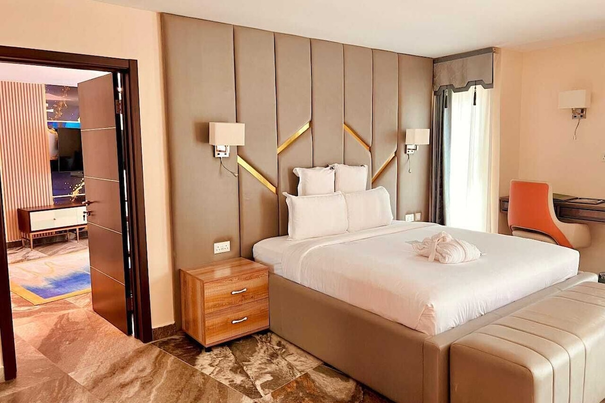 A hotel room with a large bed, a wooden nightstand, a desk, and a chair.