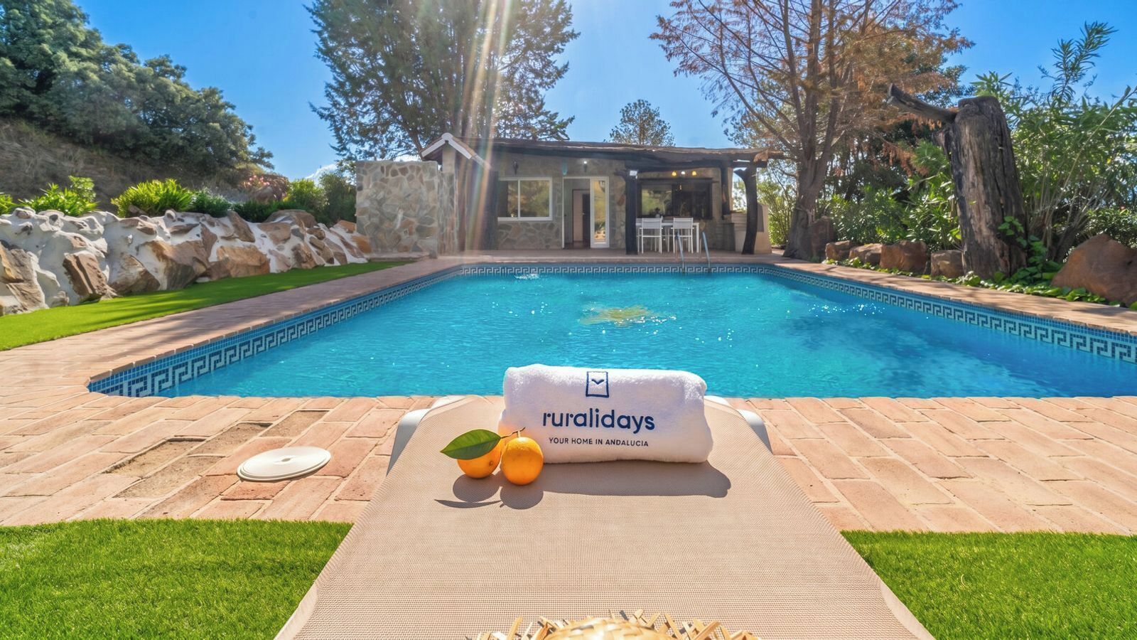 A poolside area with a lounge chair, a towel, and a sign reading 'ruralidays YOUR HOME IN ANDALUCIA.'