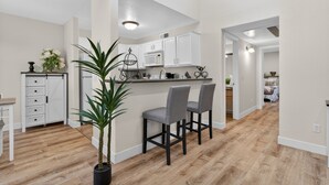 Une cuisine moderne avec des meubles blancs, un four à micro-ondes et un coin bar équipé de deux chaises.