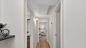 Un couloir doté d’un plancher en bois, de murs blancs et d’une bouche d’aération au plafond.