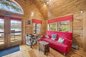 A wooden cabin with a red sofa, a patterned armchair, and a small wooden chest.