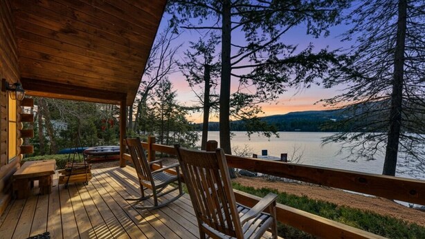 Eine Holzterrasse mit Schaukelstühlen mit Blick auf einen See bei Sonnenuntergang.