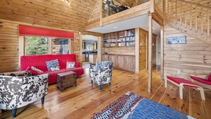 Ein Interieur einer Holzhütte mit einem roten Sofa, gemusterten Sesseln, einer Holztreppe und einer Küchenzeile.