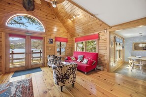 A cabin with wooden walls, a red sofa, a cowhide chair, and a dining area.