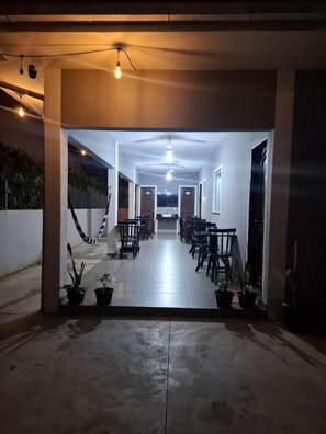 A corridor with chairs and tables, a ceiling fan, and potted plants. - Pousada canto chileno (Florianopolis)