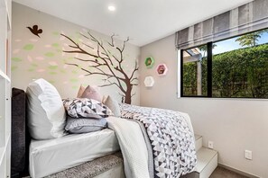 A bedroom with a bed, pillows, a geometric patterned blanket, a wall mural of a tree, and a window with a view of greenery. - Pinehill Extra-Large 8 Bedrooms House (North Shore)