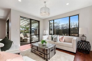 A modern living room with a white sofa, a glass door leading outside, a chandelier, and a round side table. - Pinehill Extra-Large 8 Bedrooms House (North Shore)