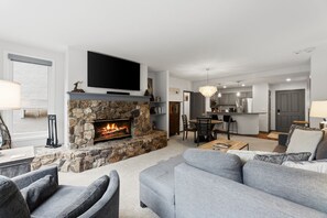 Ein Wohnzimmer mit Kamin aus Stein, einem Flachbildfernseher, grauen Sofas und einem Essbereich mit Stühlen.