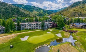 Ein Golfplatz mit Clubhaus, Teich und einem Bergpanorama.