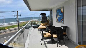 A balcony with two black wicker chairs and a cushion, a glass railing, and a view of the ocean. - CRESPO OCEAN VIEW APT (Cartagena de Indias)