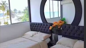 A hotel room with two beds, a large mirror, a window with a view of palm trees and the sea, and a vase with flowers. - CRESPO OCEAN VIEW APT (Cartagena de Indias)