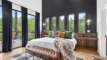 A bedroom with a large bed, a bench, a view of greenery, and a balcony.