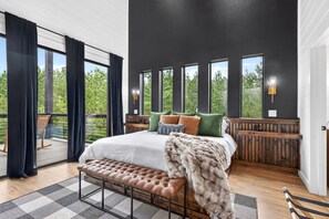 Ein Schlafzimmer mit einem großen Bett, einer Bank, Blick auf Grünflächen und einem Balkon.
