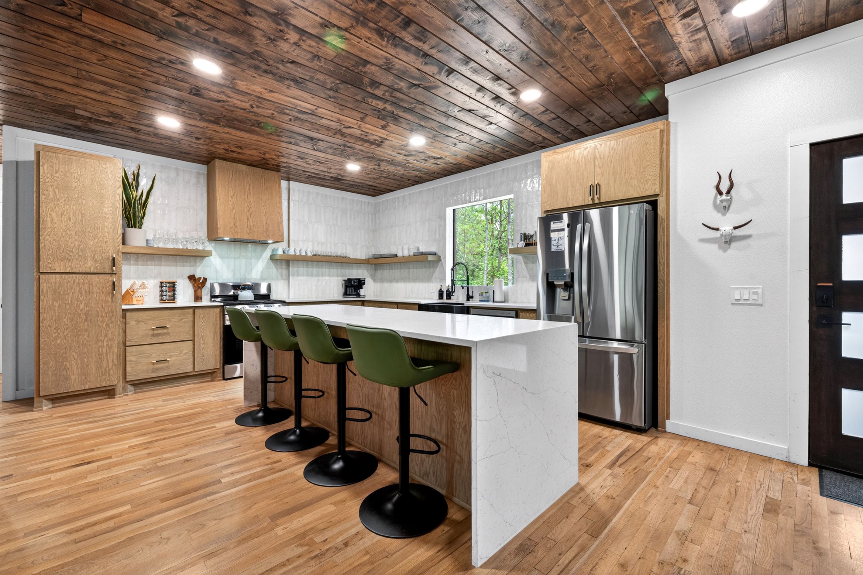 A modern kitchen with wooden cabinets, a central island with bar stools, stainless steel appliances, and a wooden ceiling.