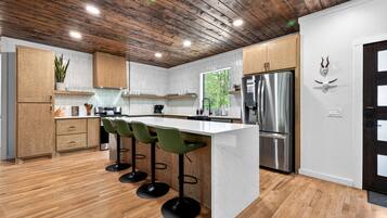 A modern kitchen with wooden cabinets, a central island with bar stools, stainless steel appliances, and a wooden ceiling.