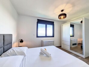 Une chambre d’hôtel avec un lit, une table de chevet, un miroir, une fenêtre et un luminaire au plafond.