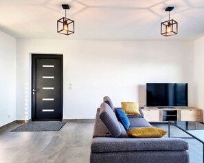 Un salon moderne avec un canapé, un téléviseur à écran plat et deux lampes suspendues.