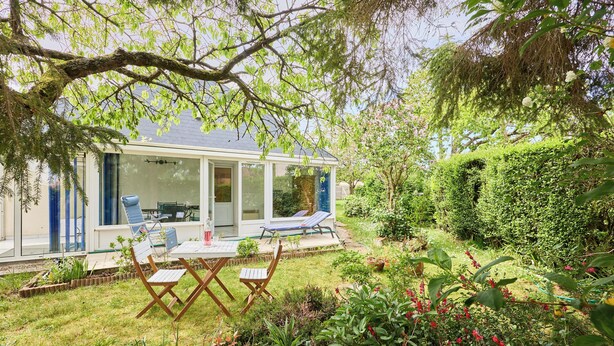 Una casa con puerta de cristal, un patio con mesa y sillas, y un jardín con diversas plantas.