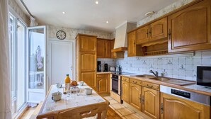 Una cocina con armarios de madera, salpicadero de azulejos, una mesa de comedor con sillas y un reloj en la pared.