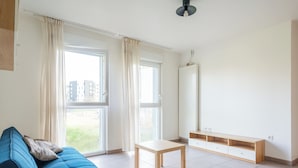 Una habitación con un sofá azul, una mesita, un espejo y una ventana con cortinas.