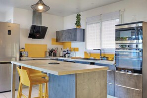 A modern kitchen with a central island, stainless steel appliances, and a yellow accent wall. - Kaz vert - Piscine - Vue mer (Saint-Pierre)