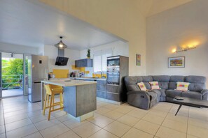 A modern kitchen with a central island, grey sofas, and a dining area with yellow chairs. - Kaz vert - Piscine - Vue mer (Saint-Pierre)