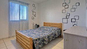 Una camera da letto con un letto in legno, un comodino, tende a una finestra e una parete con motivi geometrici.