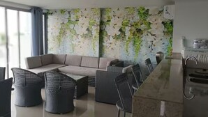 Een moderne woonkamer met een hoekbank, rieten stoelen, een eettafel en een keuken met een marmeren aanrecht.