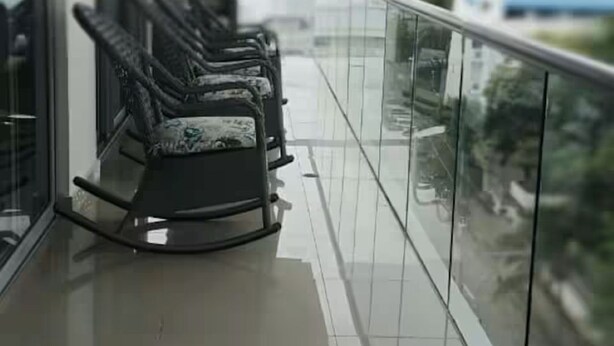 Een balkon met glazen hekwerk, een rij stoelen en uitzicht op de stad.