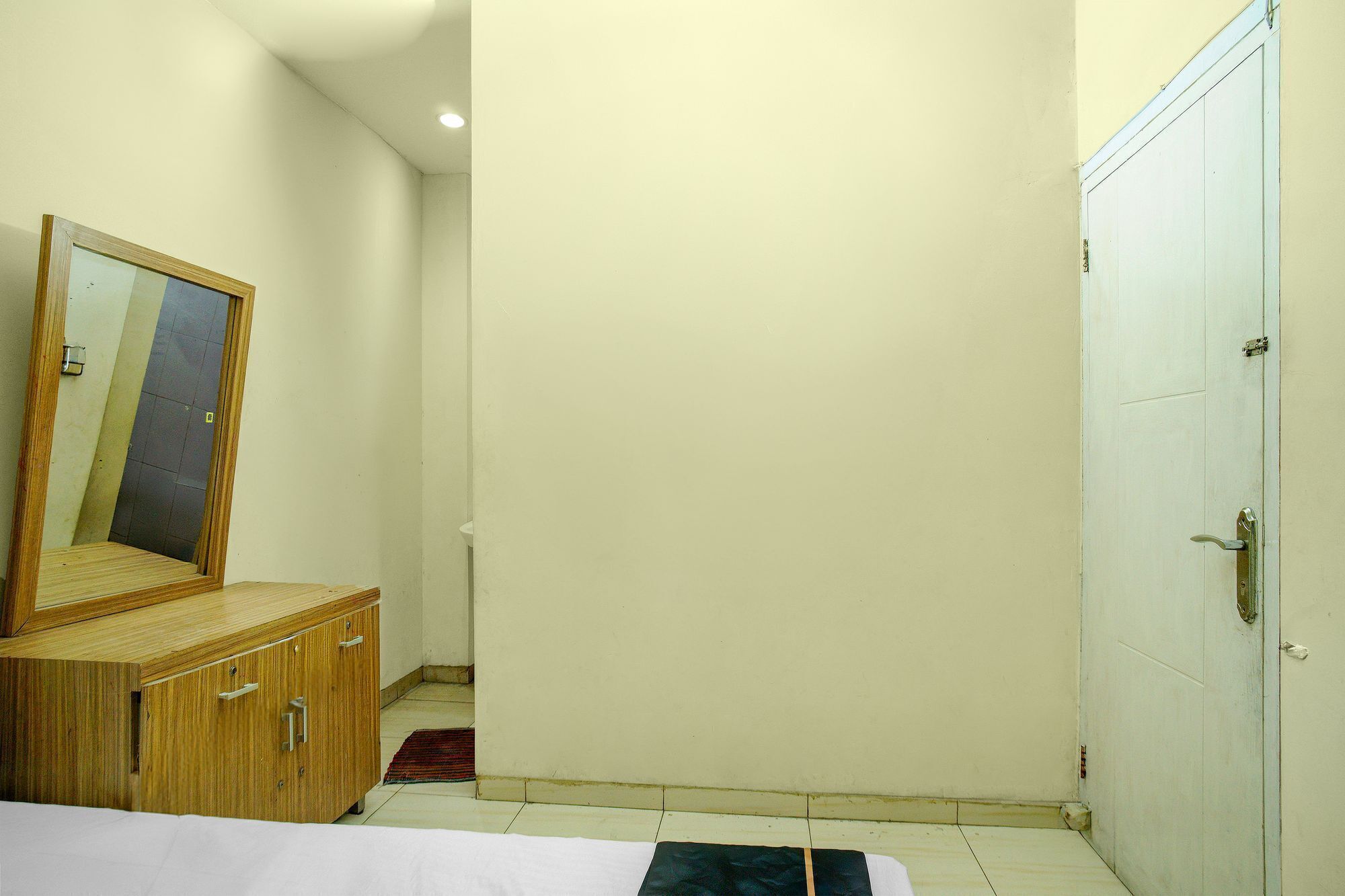 Un dormitorio con un armario de madera, un espejo, una cama blanca y una puerta.