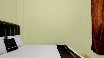 Una cama con ropa de cama blanca, un cabecero verde, una almohada negra y una cortina roja estampada.