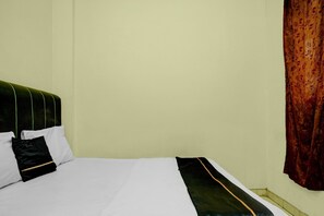 Cama com roupa de cama branca, cabeceira verde, almofada preta e cortina vermelha estampada.