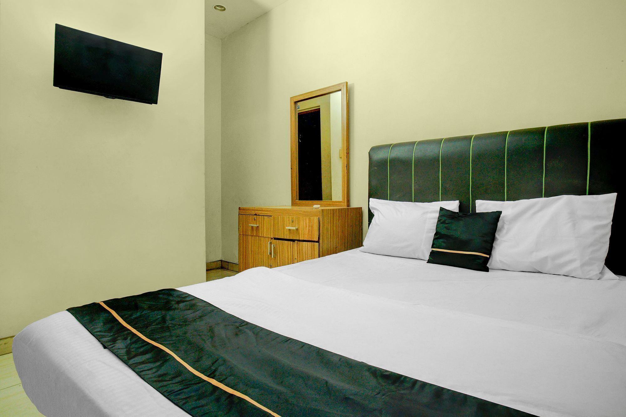 A hotel room with a bed, a wooden dresser, a mirror, and a flat-screen TV mounted on the wall.