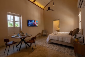 A bedroom with a bed, a TV, a dining table with chairs, and a ceiling fan. - Charming Apt Suite 3 in a Colonial House with Pool (Santa Marta)