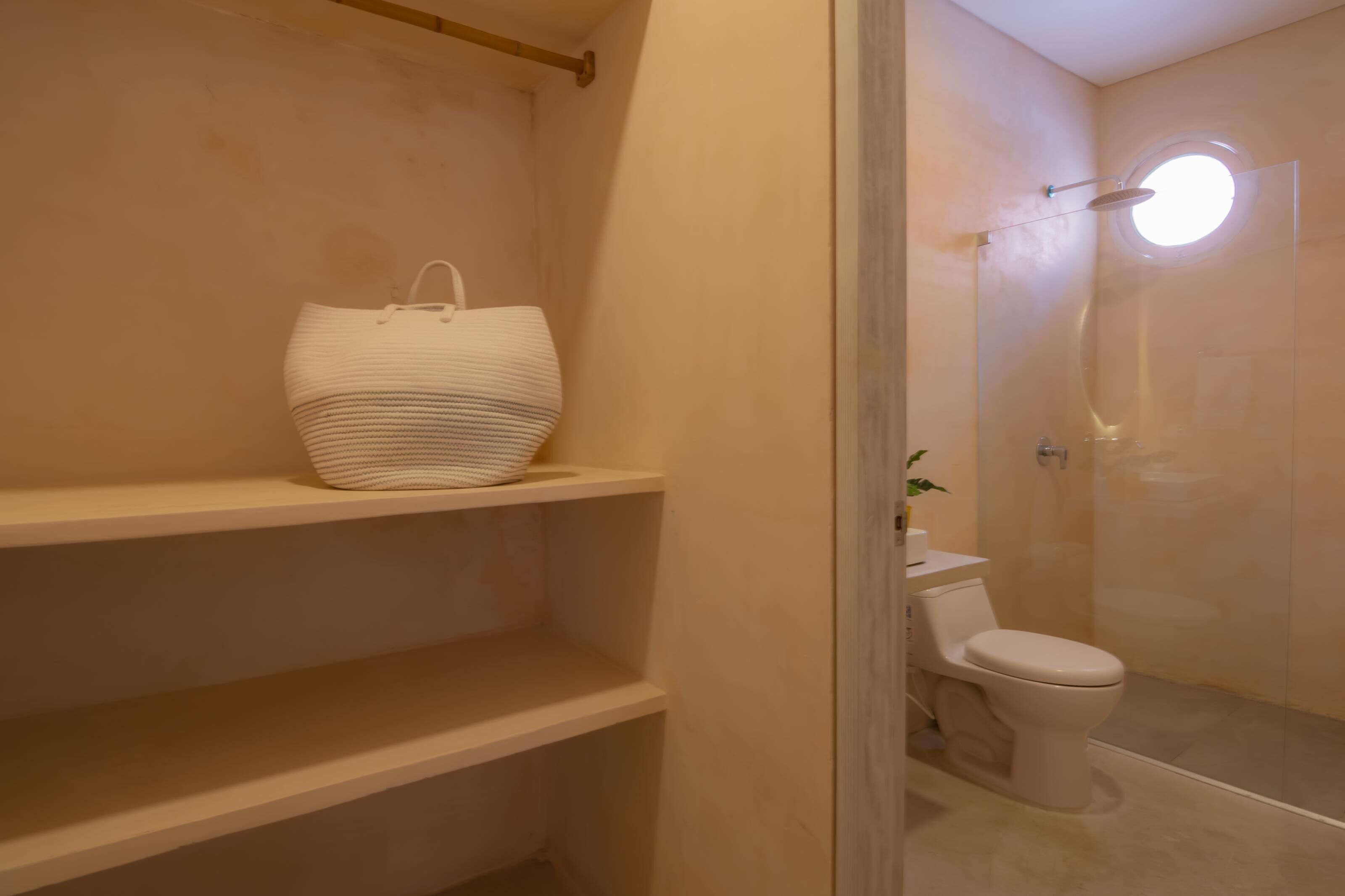 Een badkamer met een toilet, een douche en een grote, witte gevlochten mand op een plank.