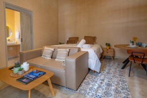A bedroom with a bed, a sofa, a small table with a book, a chair, and a bedside table with a plant. - Charming Apt Suite 5 in a Colonial House with Pool (Santa Marta)