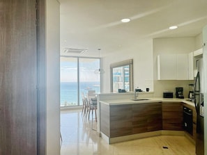 A modern kitchen with a large island, white cabinets, and a view of the ocean. - 2BR: Modern Ocean View Apartment | Grand Marina (Santa Marta)