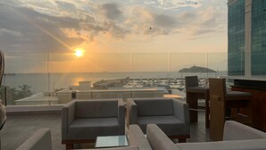 A rooftop lounge with seating and a view of the sea and cityscape during sunset. - Modern Suite with Ocean View at Gran Marina (Santa Marta)