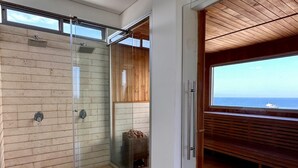 A modern bathroom with a glass shower, wooden paneling, and a view of the sea. - Modern Suite with Ocean View at Gran Marina (Santa Marta)