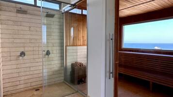 A modern bathroom with a glass shower, wooden paneling, and a view of the sea.