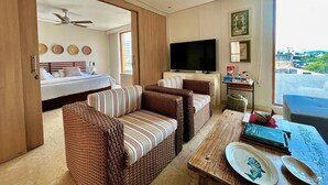 Habitación de hotel con cama, televisión, mobiliario de mimbre, una mesa de comedor con platos y vistas a la ciudad.