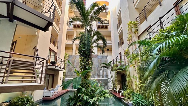 Una piscina interior de varios niveles con una cascada central, rodeada de abundante vegetación y múltiples balcones.