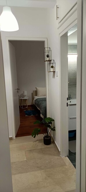 A hallway leading to a bedroom with a bed, a small table with a lamp, and a potted plant. - Marousi Accomodation 2 bedrooms (Marousi)