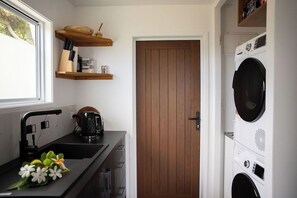A compact kitchen with a sink, a kettle, and wooden shelves above it. - MODERN STYLE VILLAS LOCATED 5 MINS TO BEST BEACH IN MURI, UNLIMITED WIFI INC (Rarotonga)