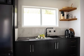 A modern kitchen with a black countertop, a double sink, and a window above the sink. - MODERN STYLE VILLAS LOCATED 5 MINS TO BEST BEACH IN MURI, UNLIMITED WIFI INC (Rarotonga)