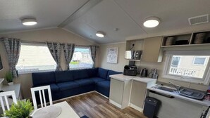 Interior compacto de autocaravana con sofá, kitchenette y ventana con vistas a un barrio residencial.