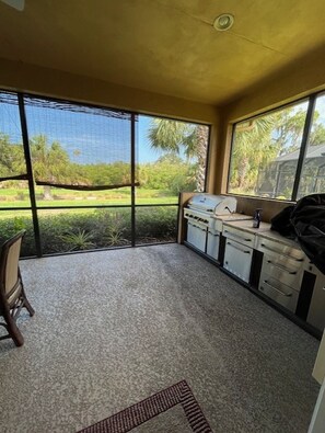 Ein Zimmer mit einer Küchenzeile, einem Sessel und Blick auf einen Garten durch große Fenster.