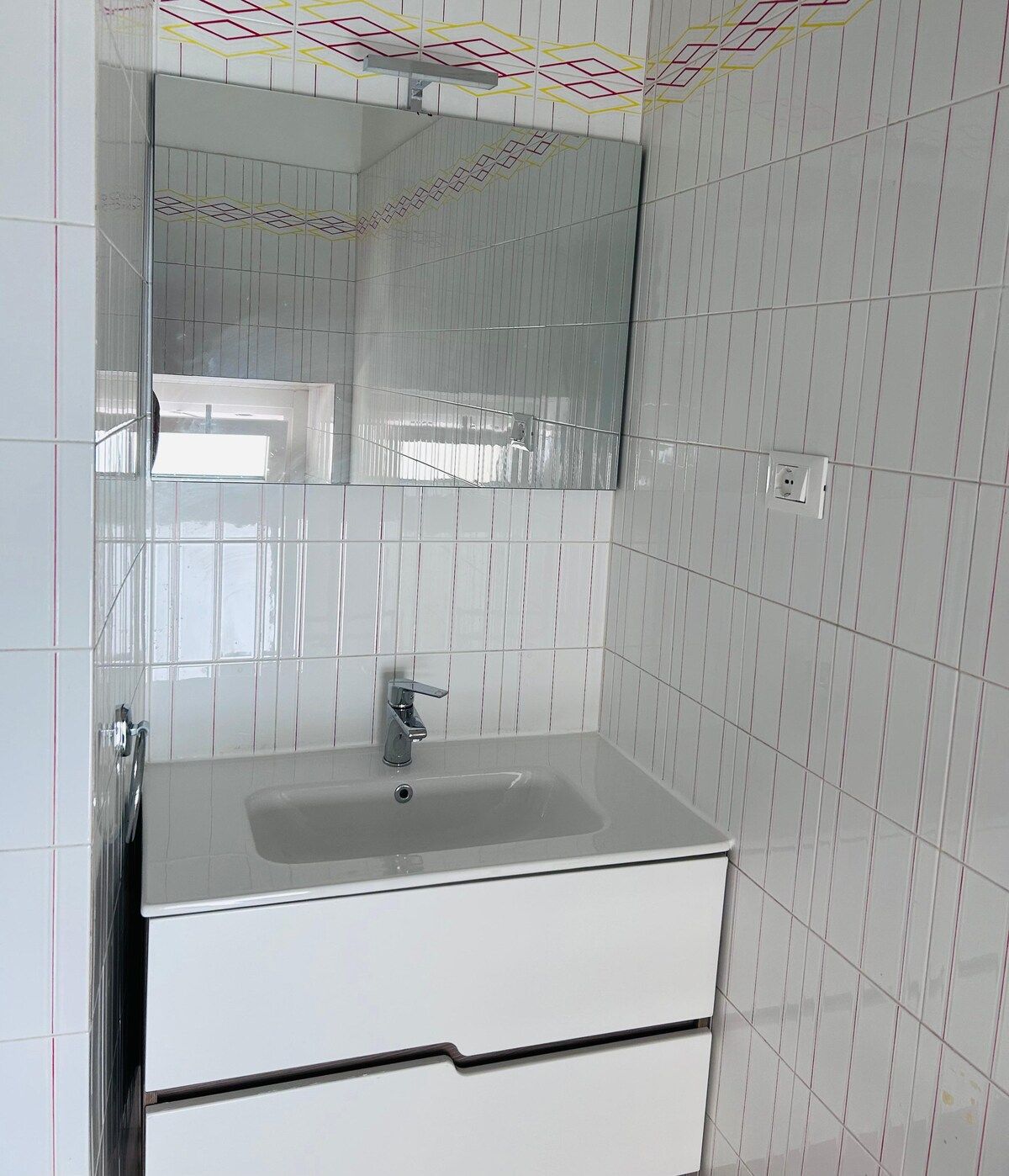A bathroom with a white sink, a mirror, and a tiled wall.