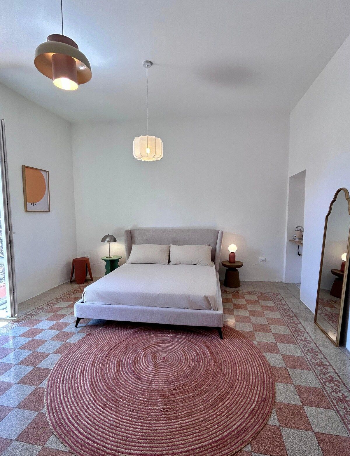 A bedroom with a bed, two bedside tables, a hanging light fixture, and a patterned rug.