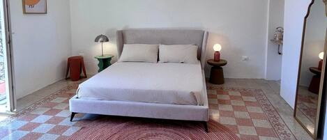 Un dormitorio con una cama, dos mesitas de noche, una lámpara colgante y una alfombra estampada.